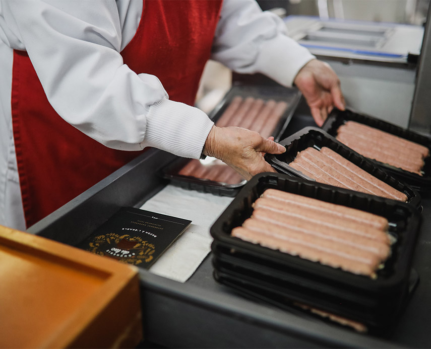 Une homme emballe des paquets de saucisses à la main